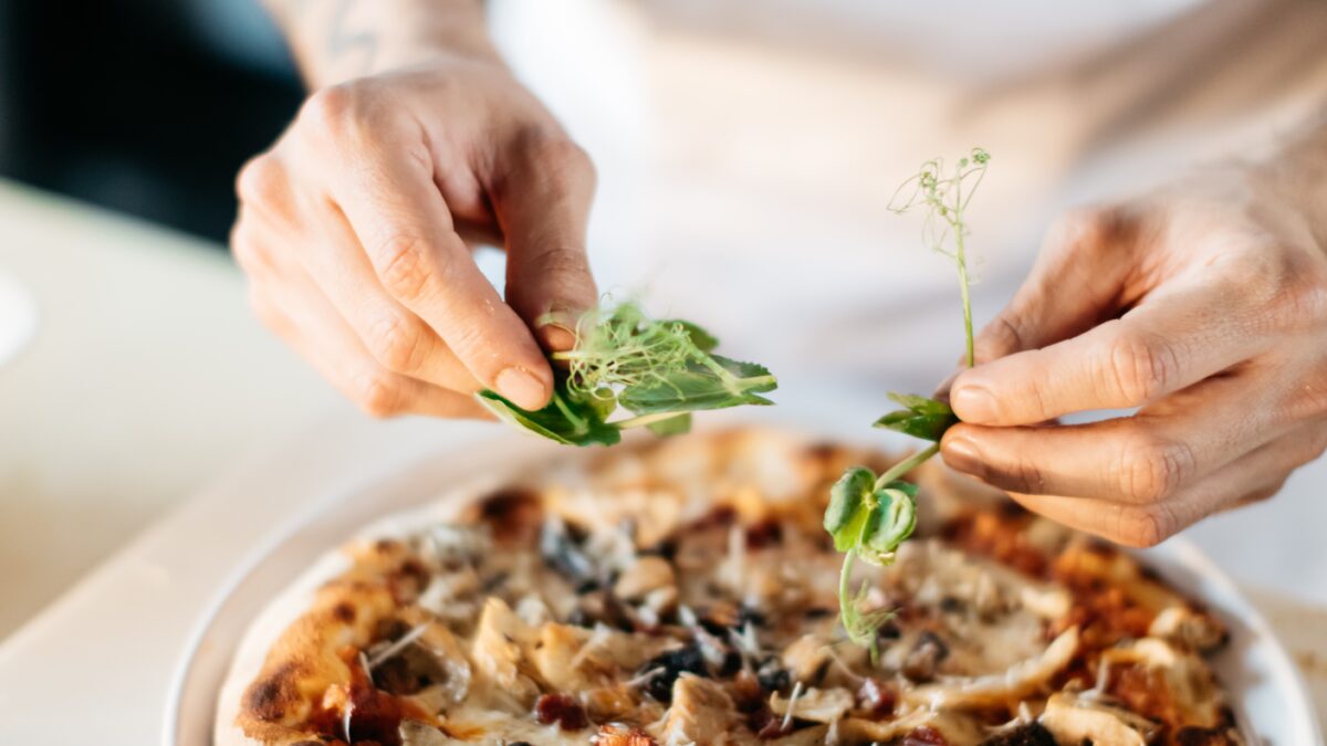 Bilden visar en person som dekorerar en pizza. Pizzaugn, elektrisk variant är ett väldigt bra val för att snabbt komma igång med pizzautbudet i din restaurang.